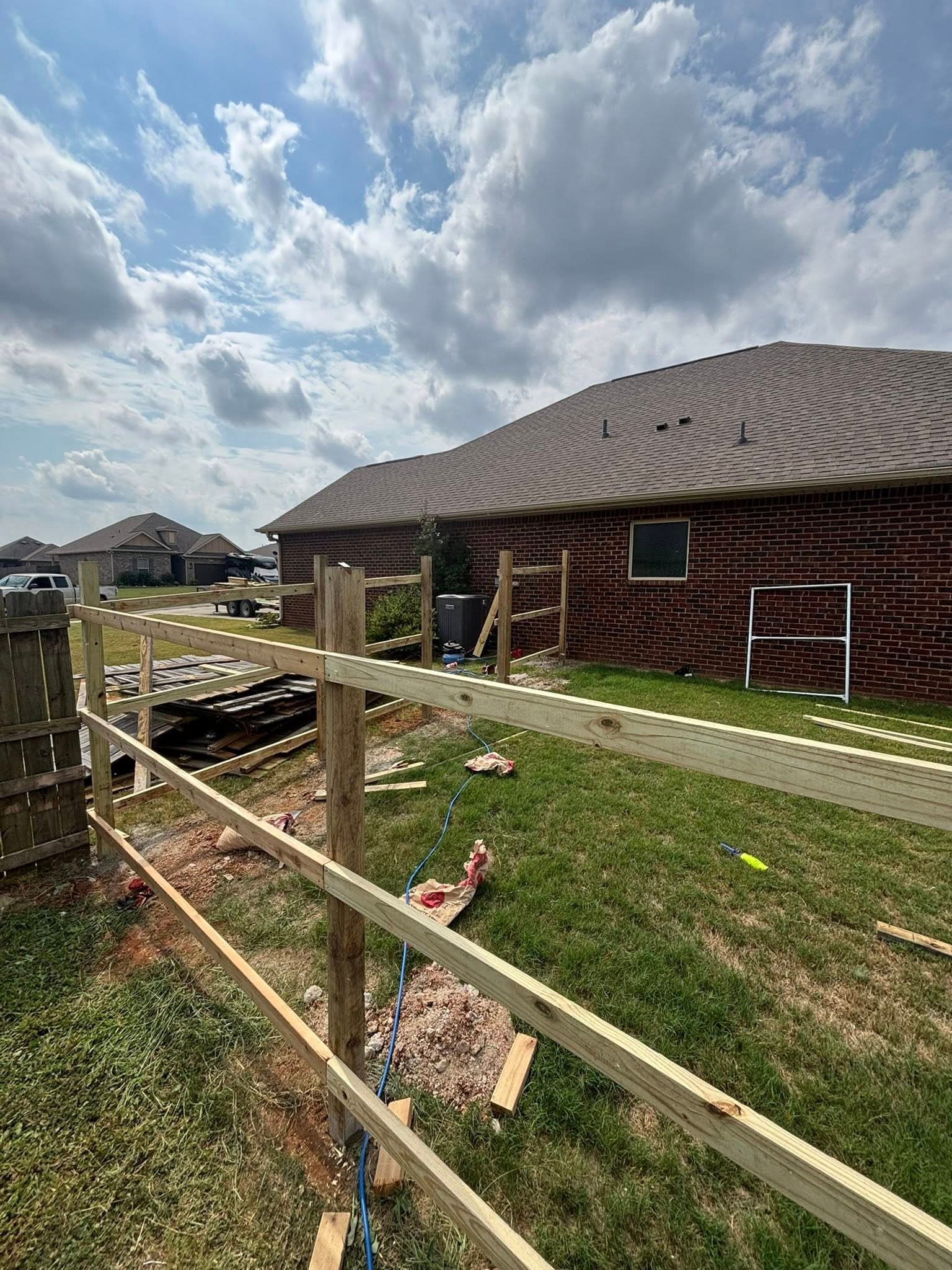 Wood fence under construction showing treated posts and horizontal rails being installed beside brick home.